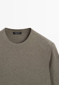 Olivgrüner Strickpullover mit strukturiertem Muster, rundem Ausschnitt und leichter Rippung am Kragen und an den Bündchen. Markenlabel innen sichtbar.