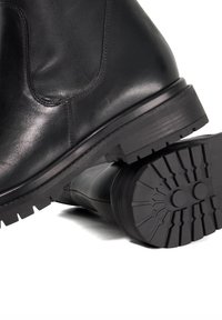 Black leather ankle boot with a smooth finish and a robust rubber sole, featuring a textured tread pattern for grip and stability.