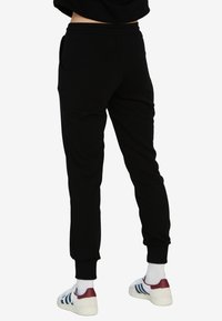 Czarne spodnie dresowe z ribbowanymi mankietami przy kostkach, bocznymi kieszeniami i miękką fakturą, w połączeniu z białymi trampkami z maroonowymi akcentami.