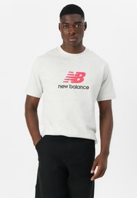 Light grey cotton t-shirt featuring a red and black "New Balance" logo. Classic crew neck design and short sleeves. Simple, casual style.