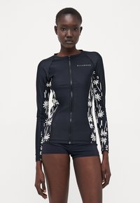 Marine langermet rash guard med hvite blomsterdetaljer, glidelås og tettsittende design. Sammen med matchende marineblå badeshorts.