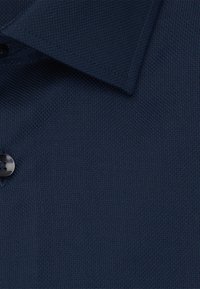 Polo shirt navy con trama testurizzata, dotato di colletto classico e un singolo bottone in plastica nera.