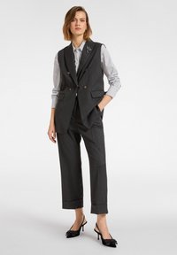 Donkergrijze op maat gemaakte gilet met een dubbele rij knopen, gecombineerd met een gestreept shirt, losse grijze broek en zwarte slingback pumps met strikken.