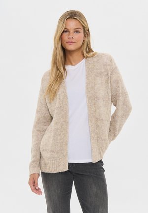 Hellbeige gestrickte Strickjacke mit offenem Vorderteil, strukturiertem Muster, gerippten Bündchen und zwei Fronttaschen, getragen über einem weißen Hemd.