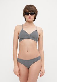 Bikini set s čierno-bielymi pruhmi s prekrývajúcim dizajnom na vrchu a zodpovedajúcimi nízko-strihanými spodkami, vyrobené z hladkej tkaniny.