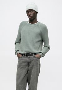 Ανοιχτό πράσινο ριγωτό πλεκτό πουλόβερ με μανίκια ράγκλαν, σετ με γκρι τζιν και γκρι πλεκτό σκούφο. Η μαύρη ζώνη προσθέτει αντίθεση.