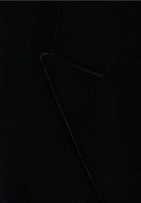 Tissu noir avec des coutures visibles mettant en valeur le bord pointu d'un revers taillé sur un manteau ou une veste.