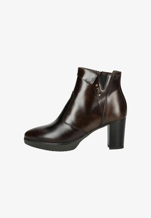 Bottine en cuir marron avec un bout pointu, des panneaux latéraux élastiques et un talon bloc texturé. Présente un petit accent métallique près de la cheville.