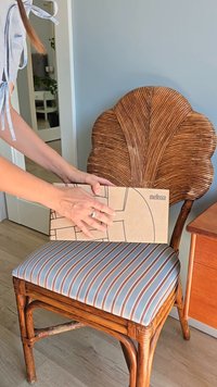 Caja de cartón marrón con un diseño geométrico y etiqueta "melissa", colocada sobre una silla acolchada a rayas azules y blancas con respaldo de madera trenzada.