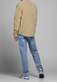 Beżowa koszula z długim rękawem, luźny krój. Jasnoniebieskie jeansy z efektem sprania. Szare buty sportowe z białymi akcentami i czarnymi detalami.