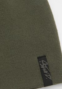 Maslinasto zelena pletena zimska kapa s rebrastom teksturom; sadrži crnu oznaku s stiliziranim logotipom. Pogodna za svakodnevno nošenje u hladnom vremenu.