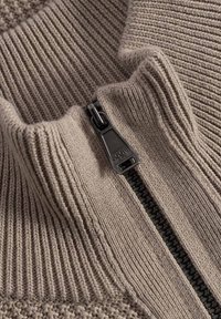 Beige tröja med hög krage och dragkedjestängning. Texturerad stickning med ribbad detalj och en slät dragkedja som accent.