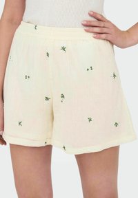 Pantalones cortos de color amarillo claro hechos de una tela texturada, con bordados florales verdes esparcidos por la superficie y una cintura elástica.