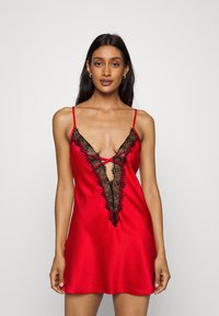 Red satin nightdress featuring a deep V-plunge neckline with black lace trim and crisscross detailing, finished with thin shoulder straps.