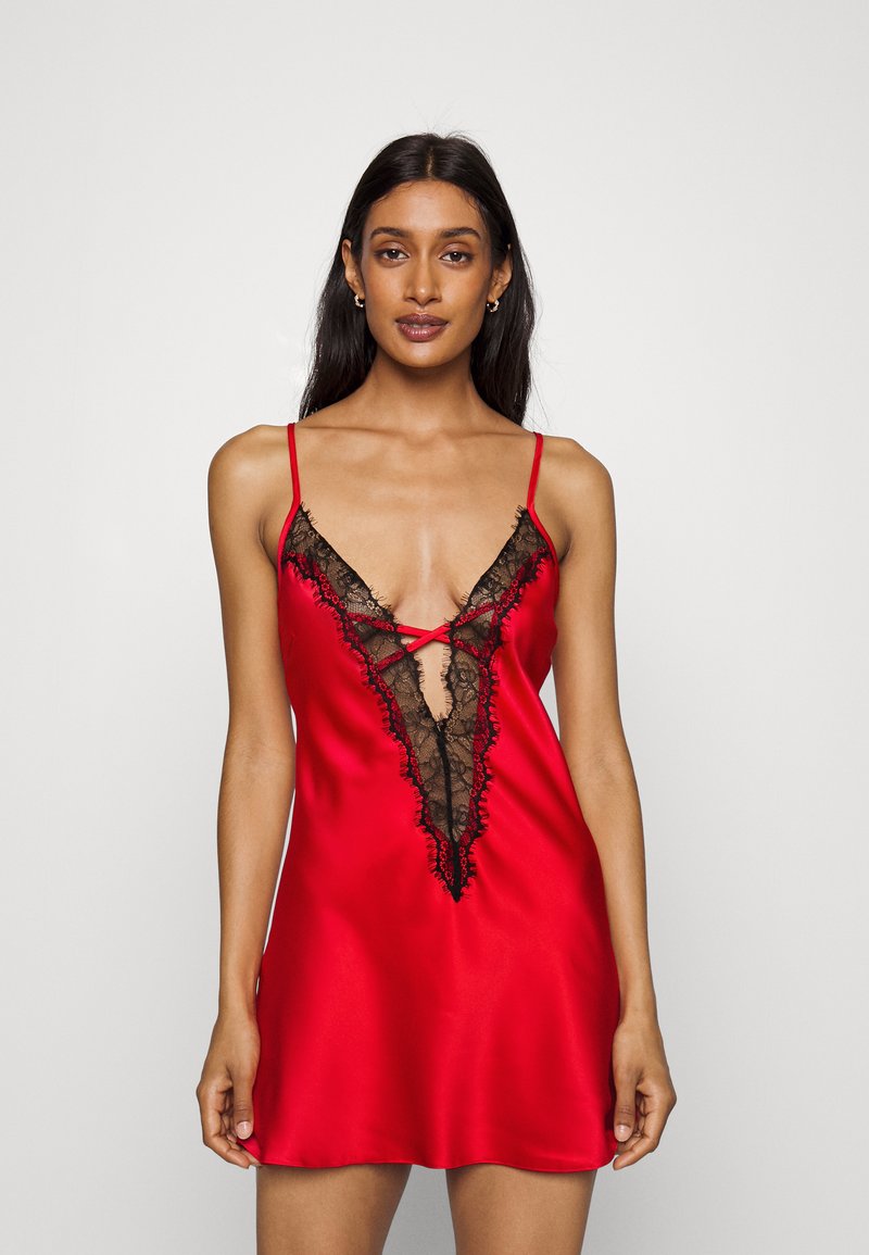 Red satin nightdress featuring a deep V-plunge neckline with black lace trim and crisscross detailing, finished with thin shoulder straps.