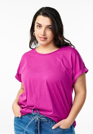 Camiseta casual fucsia con mangas cortas enrolladas, escote redondo y textura suave y lisa. Llevada con pantalones cortos de mezclilla de tiro alto.