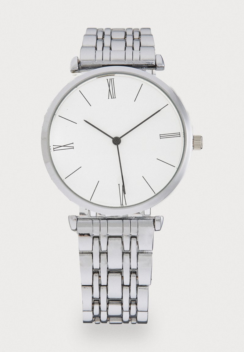Ezüst fém óra kerek számlappal, fehér dísszel, fekete római számokkal, két fekete mutatóval és texturált láncszíjjal.