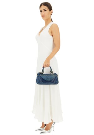 Borsa in pelle blu con dettagli borchiati, forma arrotondata e doppio manico. Indossata con un abito bianco e decolletè argento, mette in risalto linee eleganti.