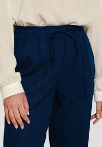Marineblauwe linnenmix broeken met een elastische tailleband en trekkoord. Met zijzakken en een relaxte pasvorm, gecombineerd met een beige shirt.