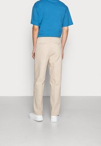 Pantaloni khaki a gamba dritta con vestibilità rilassata. Realizzati in cotone, presentano due tasche posteriori con bottoni visibili. Abbinati a una maglietta blu.