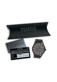 Montre ronde noire avec des index en rose doré, bracelet en cuir et cadran noir mat. Comprend un emballage noir et une carte de garantie.
