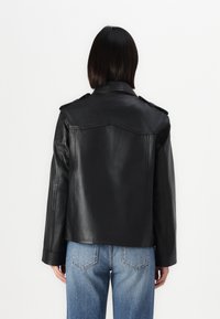 Svart skinnjakke med klassisk design, med skulderklaffer og en glatt tekstur. Båren over blå denimjeans.