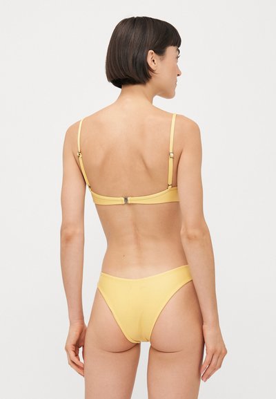Completo bikini giallo con spalline sottili, un design elegante e una chiusura semplice sul retro. Il tessuto appare liscio e elastico.