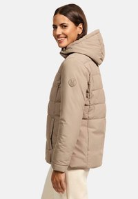 Beige pufferjack met een capuchon, voorzien van een getailleerd ontwerp, een logo op de mouw en voorzakken. Gladde textuur met een aansluitende pasvorm.
