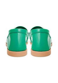 Par grønne læder loafers med lysebrune flade såler vist bagfra på hvid baggrund.