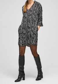 Svart och vit mönstrad klänning med V-hals, trekvartslånga ärmar och sidfickor, kombinerad med knähöga svarta läderstövlar.