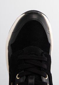 Gros plan sur le bout d'une basket noire avec des panneaux en cuir et en daim, des lacets noirs et une semelle en caoutchouc blanche.