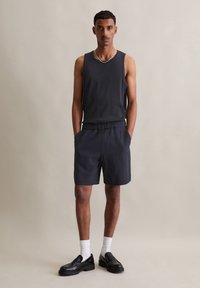 Heren lichtgewicht donkergrijze tanktop en bijpassende shorts, met een comfortabele pasvorm, elastische tailleband en zakken, gecombineerd met zwarte schoenen.