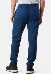 Blaue, strukturierte Jogginghosen mit einem Kordelzugbund, schlankem Schnitt, Gesäßtasche und gerippten Bündchen, kombiniert mit schwarzen Sportschuhen.