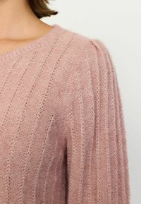 Roze gebreide trui met geribbelde structuur en subtiele strepen. Heeft een ronde halslijn en licht gepofte schouders. Zacht, lichtgewicht materiaal.