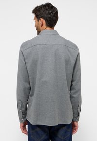 Graues Hemd mit Knopfleiste und langen Ärmeln, strukturierter Stoff, abgerundeter Saum und kontrastierende Nähte. Knöpfe an den Manschetten sichtbar.