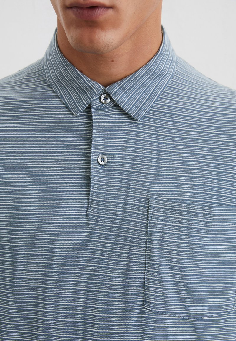Helles blaues Polohemd mit weißen Streifen, taillierter Kragen, zwei-Knopf-Leiste und einer Brusttasche. Weicher Stoff mit glatter Textur.