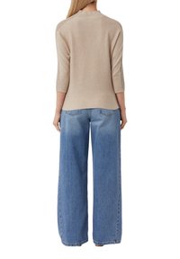 Beige gebreide top met hoge hals en driekwartmouwen, gedragen met losse, lichtblauwe wijde jeans met achterzakken.