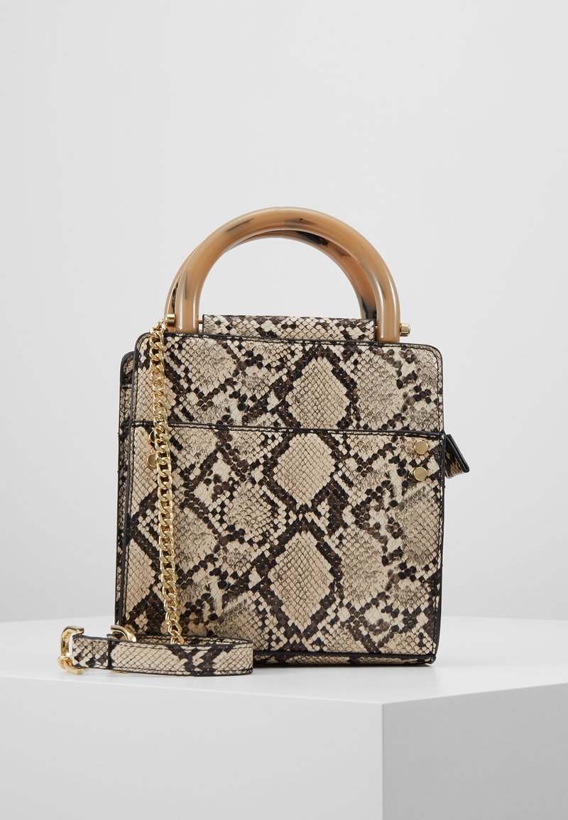 Sac carré avec imprimé serpent beige et noir, bandoulière en chaîne dorée et poignée supérieure incurvée beige translucide sur surface blanche.