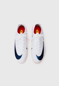 Een paar witte sportschoenen met zwarte swoosh-logo's, witte veters en rode binnenzolen met gele details, van boven bekeken op een witte achtergrond.
