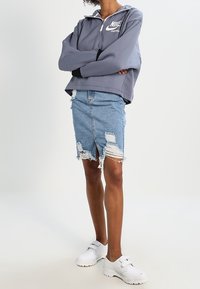 Grå överhuvudströja med vit Nike-logotyp och halv dragkedja, tillsammans med en slitna denimkjol med fransig söm och vita sneakers.