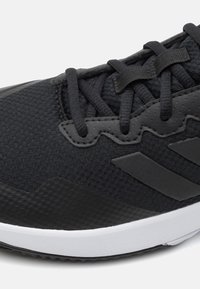 Närbild av svart sportskor med texturerat tyg, svarta snörningar och en vit sula.