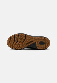 Semelle de chaussure de sport noire avec un motif texturé, présentant des grips en caoutchouc au design en nid d'abeille, contrastant des couleurs marron clair et foncé.