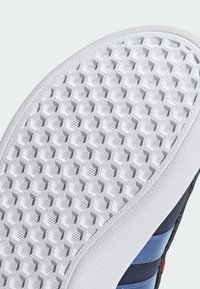 Witte rubberen schoenzool met hexagonaal profiel en blauw stoffen bovenwerk gedeeltelijk zichtbaar op een lichte achtergrond.