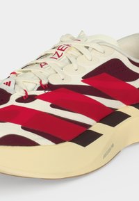 Άσπρα και βυσσινί αθλητικά παπούτσια Adidas με κόκκινες ρίγες, λευκά κορδόνια και ετικέτα "LIGHTSTRIKE PRO" στη ανοιχτόχρωμη σόλα.