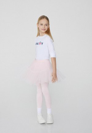 Witte langekous overhemd met "ENJOY" graphic en aardbei, gecombineerd met een lichtroze tule rok, witte leggings en witte sneakers.