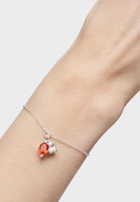 Pulsera de cadena de plata que presenta un cristal redondo naranja y dos pequeños acentos de plata. La pulsera se lleva en un tono de piel claro.