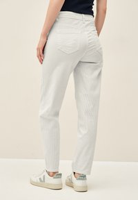 Pantalones de pana de color gris claro con corte recto, que cuentan con bolsillos traseros y se combinan con zapatillas blancas y grises. Textura suave, diseño casual.