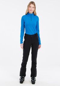 Blå långärmad tröja med halvdragkedja, matchad med svarta skidbyxor med sidofickor med dragkedja och en figurnära midja. Svarta skidstövlar.