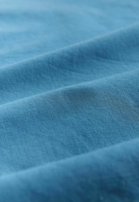 Tissu bleu texturé avec une finition mate et lisse, présentant de subtiles variations de couleur et de légers plis, indiquant une certaine souplesse.