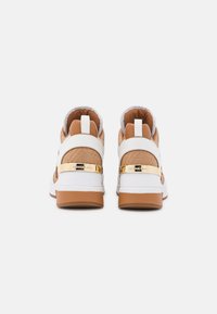 Sneakers bianchi e beige con tomaia in tessuto testurizzato, dettagli in metallo dorato e suola in gomma marrone. La vista posteriore mostra il collare imbottito e il marchio.